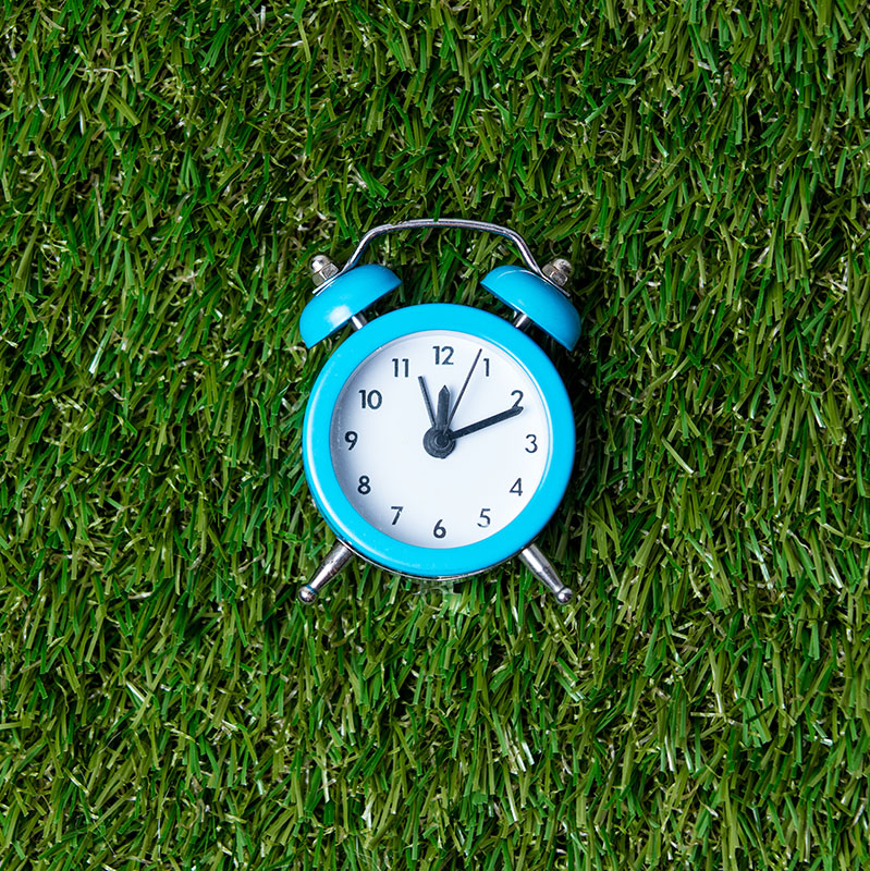 blue-little-retro-alarm-clock-on-green-grass-backg